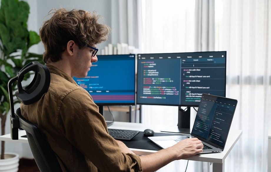 developer sitting in front of laptop with several displays in the background
